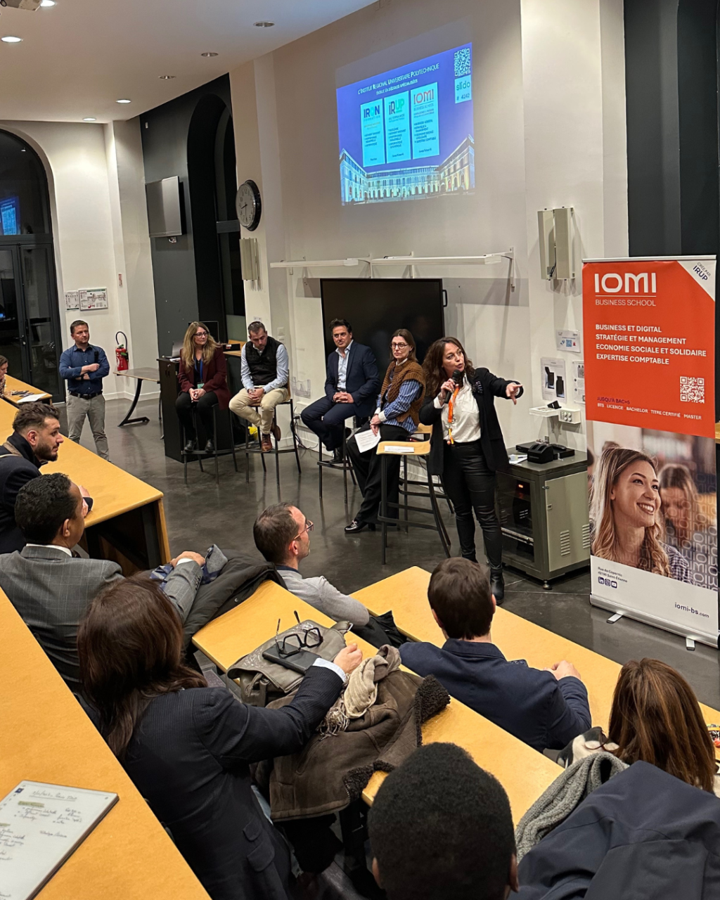 IOMI reçoit ses entreprises partenaires : intervenante et panel en amphithéâtre, bannière IOMI à droite